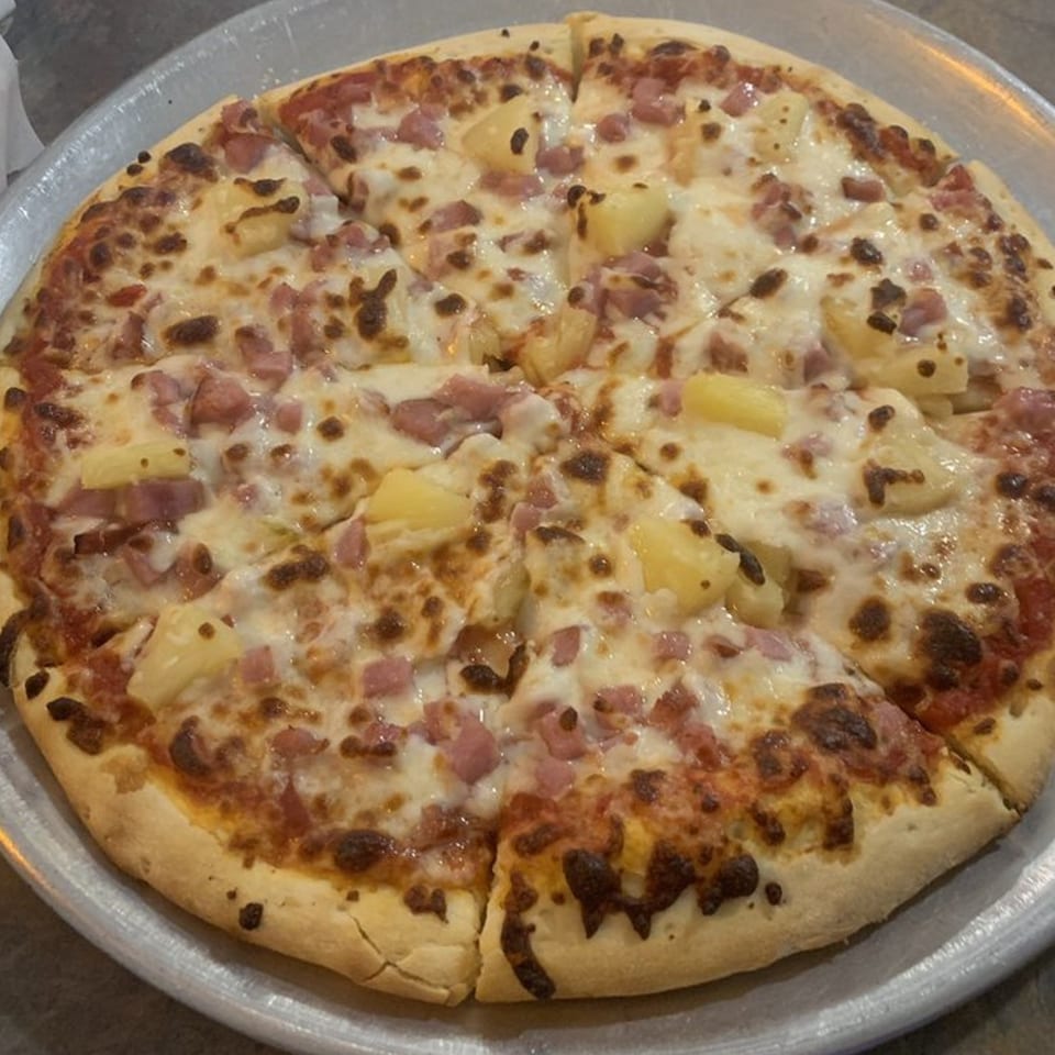 A whole Hawaiian pizza with ham and pineapple, sliced and ready to eat on a metal tray.