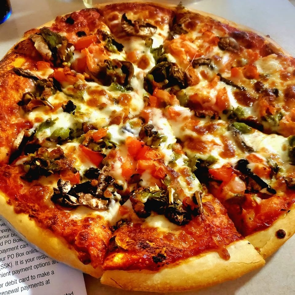 A whole pizza from Socorro's Restaurant, topped with melted cheese, tomatoes, mushrooms, and green peppers.